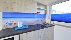 A kitchen with a wooden cabinet, a blue countertop, a coffee maker, and a window with a view of buildings. - Comfortable holiday homes with a summer pool (Jaroslawiec)