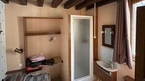 Une chambre à coucher comprenant un lit, une table de chevet, une armoire, une salle de bain avec un lavabo et un miroir, et une fenêtre avec des rideaux.