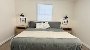 A bedroom with a bed, two bedside tables, a window with blinds, and two wall-mounted lamps. - 3-bedroom House, Private Lake Access and Game Room (Hillsboro)