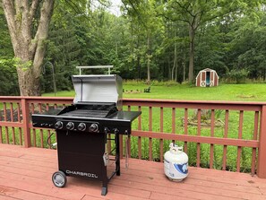 A Charbroil grill on a wooden deck with a propane tank nearby, surrounded by a wooded area. - 3-bedroom House, Private Lake Access and Game Room (Hillsboro)