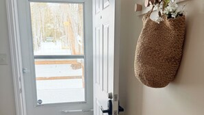A door with a view of a snowy landscape, a wooden floor, and a wall-mounted shelf with a woven bag and a small plant. - 3-bedroom House, Private Lake Access and Game Room (Hillsboro)
