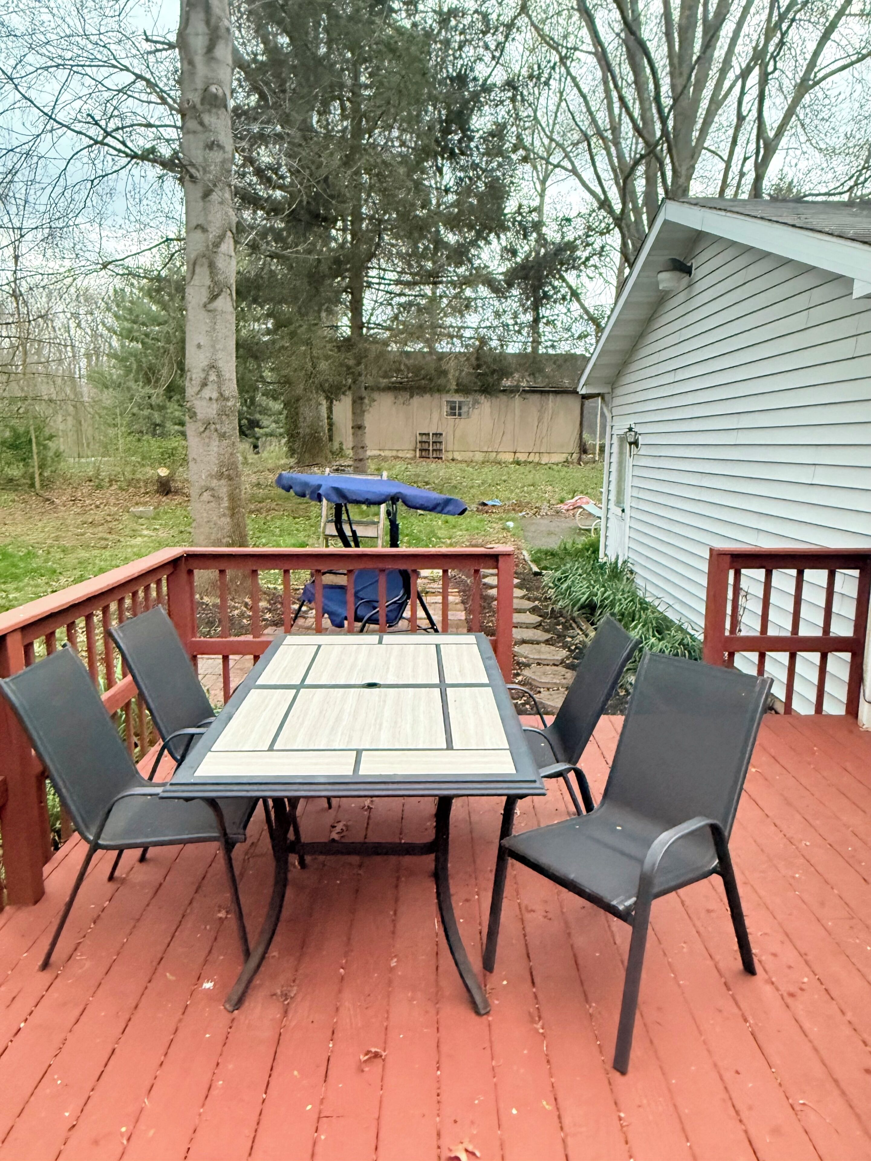 Eine Holzterrasse mit Tisch und Stühlen, einem blauen Sonnenschirm und einem Haus im Hintergrund.