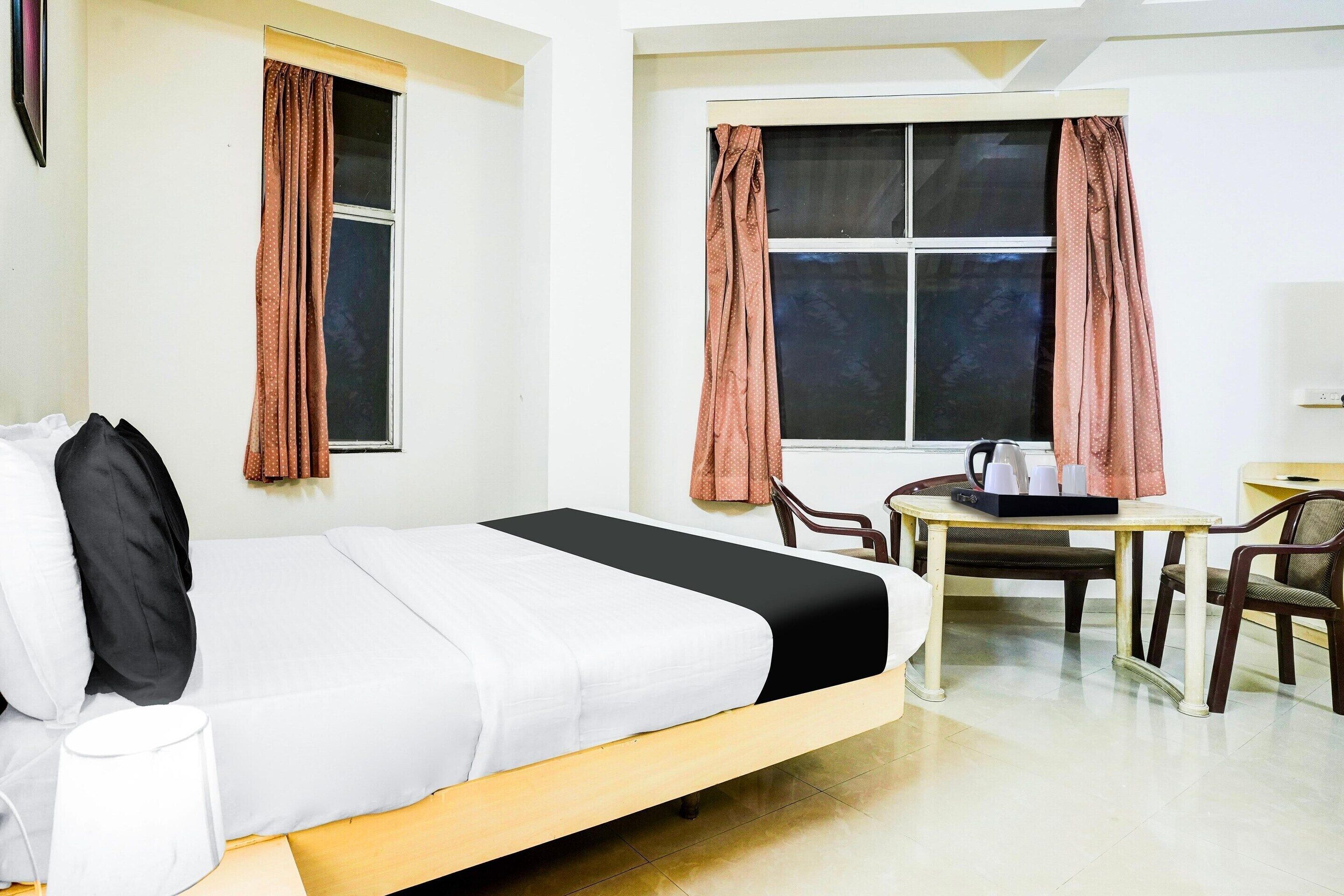 Une chambre d’hôtel comprenant un lit, un bureau avec des chaises, une fenêtre avec des rideaux et un téléviseur fixé au mur.