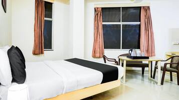 Une chambre d’hôtel comprenant un lit, un bureau avec des chaises, une fenêtre avec des rideaux et un téléviseur fixé au mur.