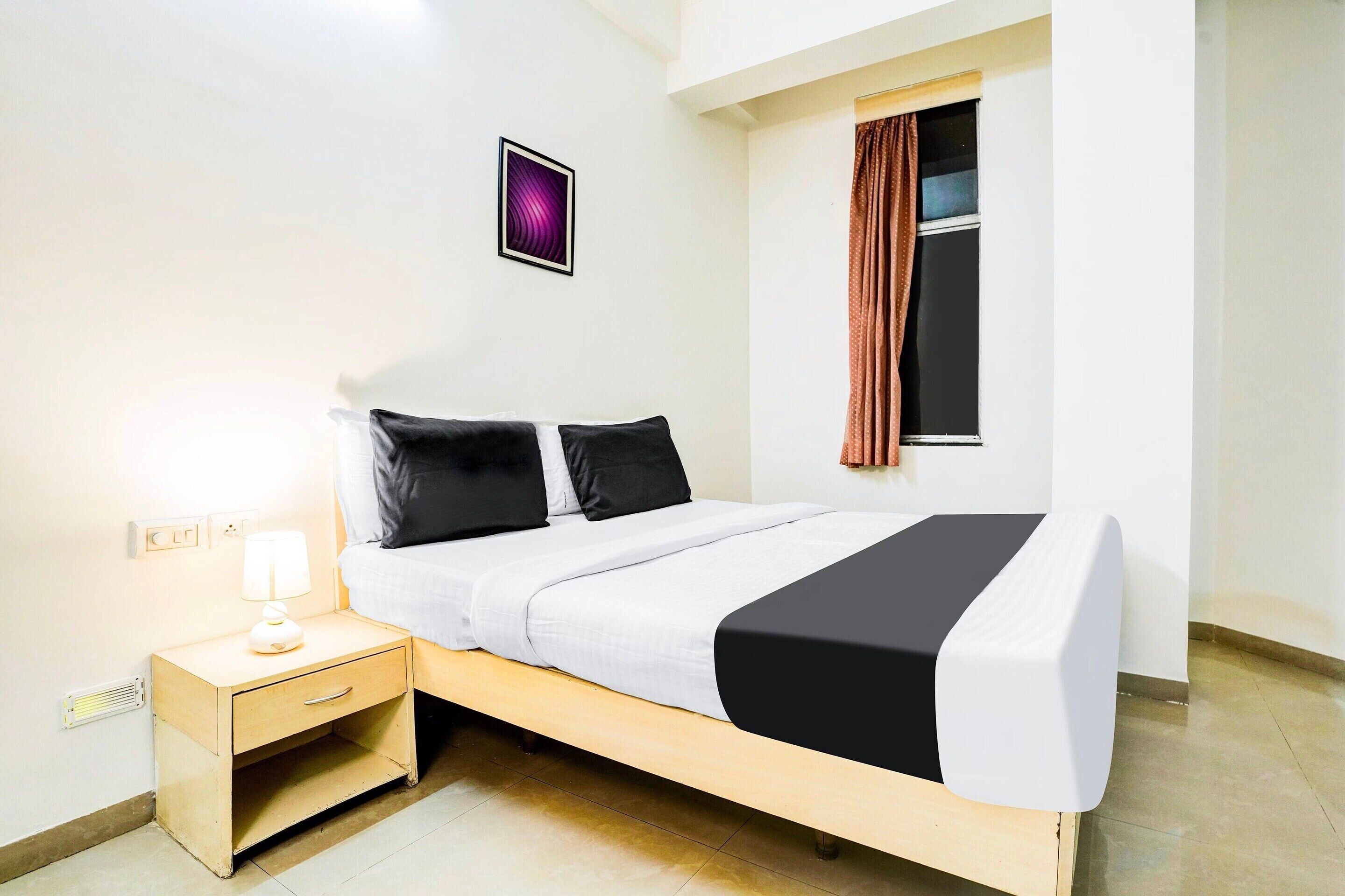 A single bed with a white and black bedspread, a bedside table with a lamp, and a window with curtains.