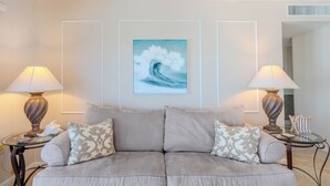 A living room with a beige sofa, two lamps, a framed painting, and a glass coffee table. - 🏖️Water Views | Steps to Beach | Beachfront Complex | Island Winds Penthouse 1 (Fort Myers Beach)
