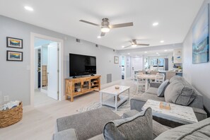A modern living room with a television, sofa, coffee table, and ceiling fans. - ☀️Beachfront with Great Views | Gorgeous Interior | Carlos Pointe #425🌴 (Fort Myers Beach)