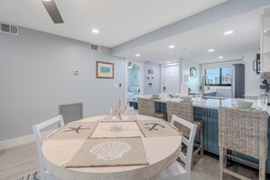 A dining area with a round table, wicker chairs, and a view into the kitchen. - ☀️Beachfront with Great Views | Gorgeous Interior | Carlos Pointe #425🌴 (Fort Myers Beach)