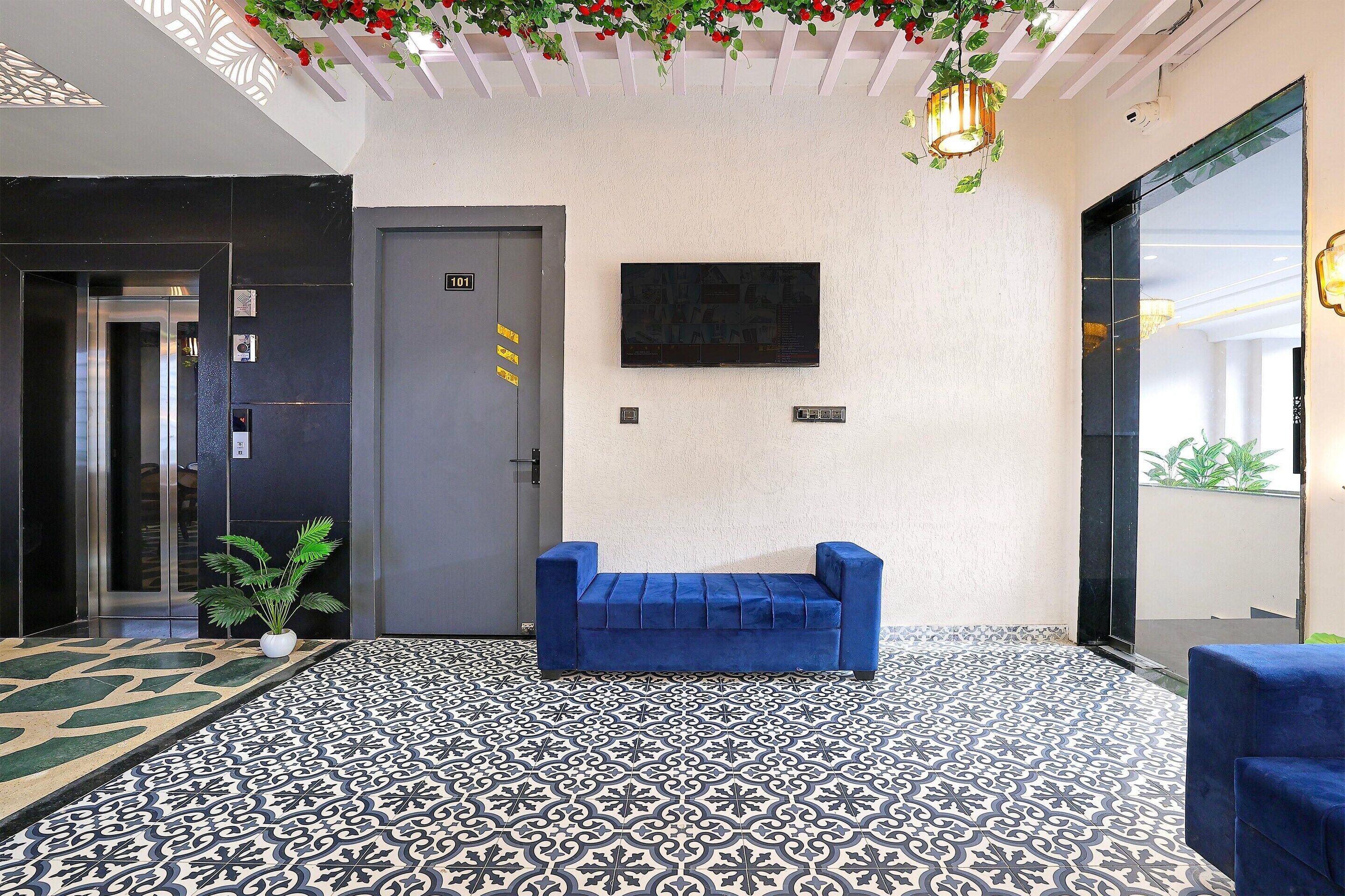 A lobby with a patterned floor, a blue sofa, a door marked 101, and a wall-mounted TV.