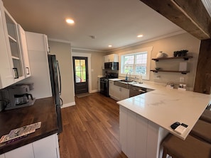 Una cocina moderna con armarios blancos, piso de madera, una isla grande con horno integrado y una ventana que proporciona luz natural.