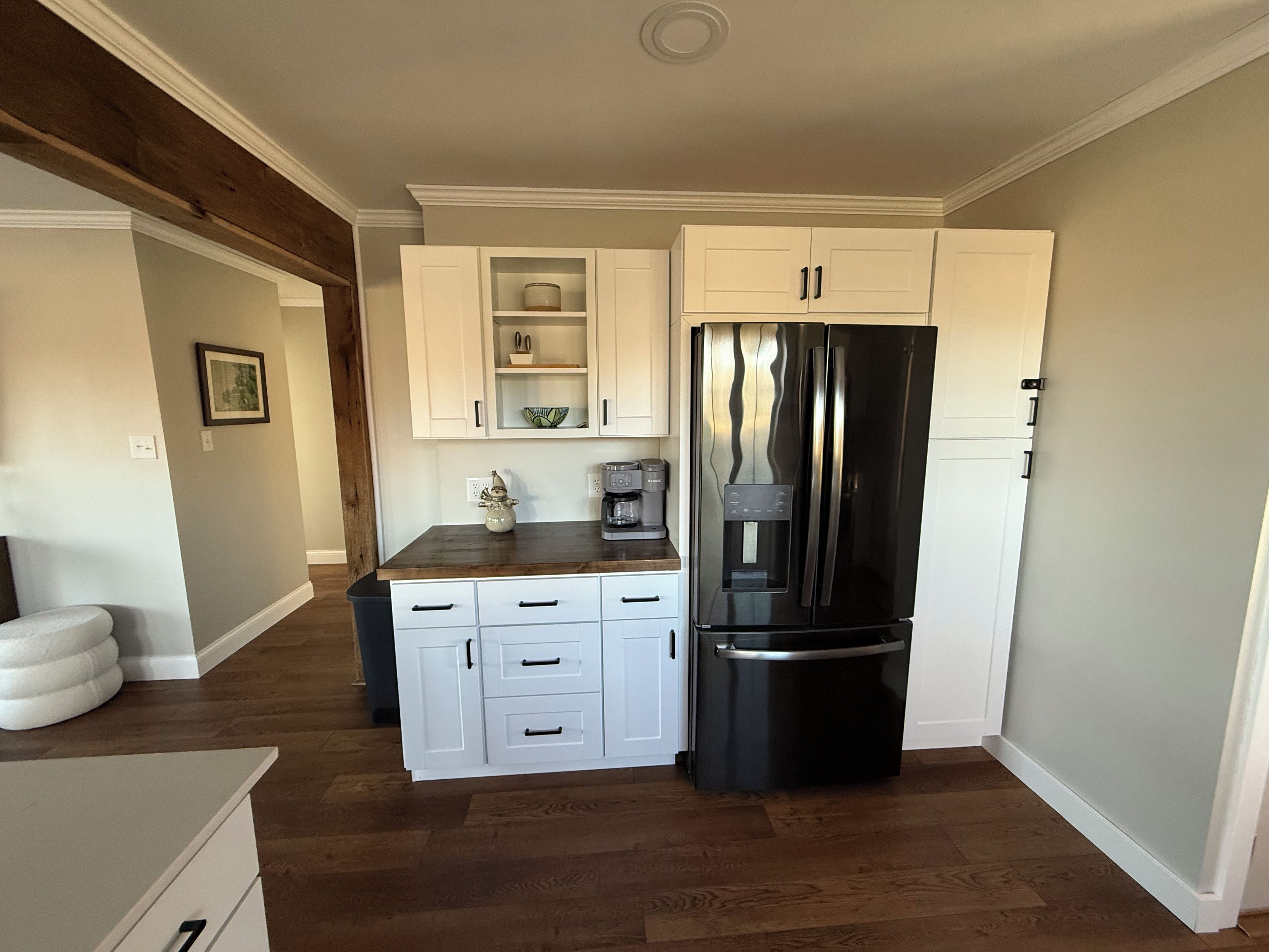 A compact kitchen with white cabinetry, a black refrigerator, and a wooden countertop.