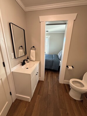 A bathroom with a sink, mirror, toilet, and a doorway leading to a bedroom. - Pa’s House is an enjoyable, entirely remodeled, 2-bedroom farmhouse near Anna. (Anna)