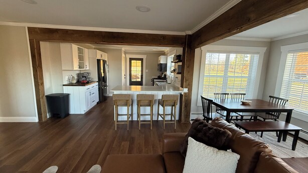 A spacious living room with a brown leather sofa, a dining area with a wooden table and chairs, a kitchen with white cabinets and a central island, and large windows with blinds. - Pa’s House is an enjoyable, entirely remodeled, 2-bedroom farmhouse near Anna. (Anna)