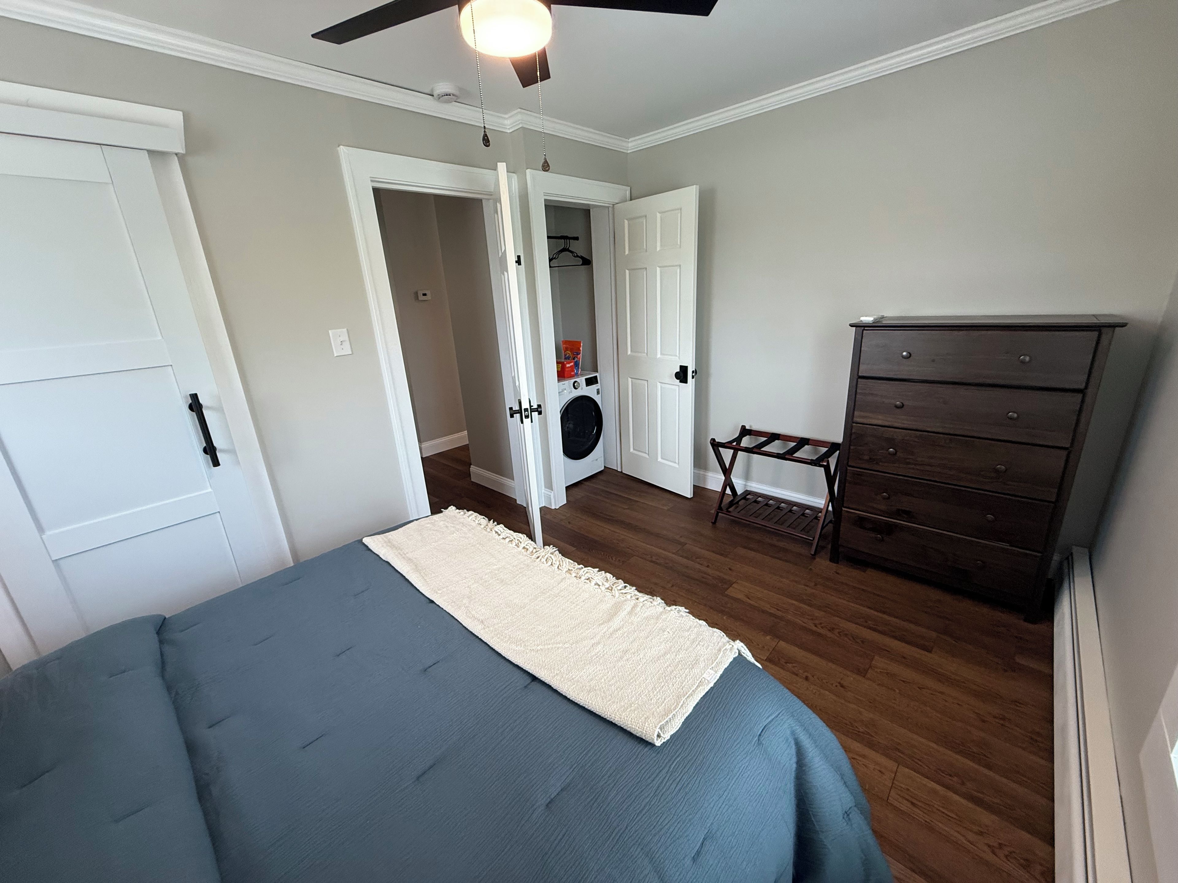 A bedroom with a bed, a dresser, a ceiling fan, and a door leading to a laundry area.