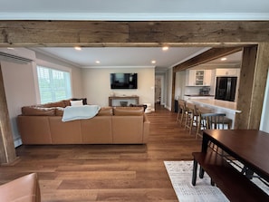 A modern living room with a brown leather sofa, a wooden dining table, and a kitchen area with white cabinets and a stainless steel refrigerator. - Pa’s House is an enjoyable, entirely remodeled, 2-bedroom farmhouse near Anna. (Anna)