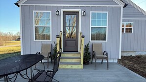 A house with a grey exterior, a front porch with a table and chairs, and a small staircase leading to the entrance. - Pa’s House is an enjoyable, entirely remodeled, 2-bedroom farmhouse near Anna. (Anna)