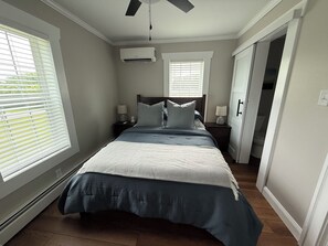 Une chambre à coucher comprenant un lit, des tables de chevet, un ventilateur de plafond et un appareil de climatisation.