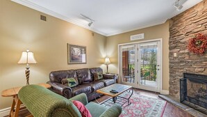 A living room with a leather sofa, a green armchair, a coffee table, and a fireplace. There is a door leading outside and a framed picture on the wall. - 🌄 Baskins Creek 110 - Private Balcony - Fireplace - Steps to Downtown 🏔 (Gatlinburg)