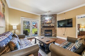 Ein Wohnzimmer mit Kamin aus Stein, einem flachbildfernseher an der Wand und einem Sofa mit gemusterten Kissen.
