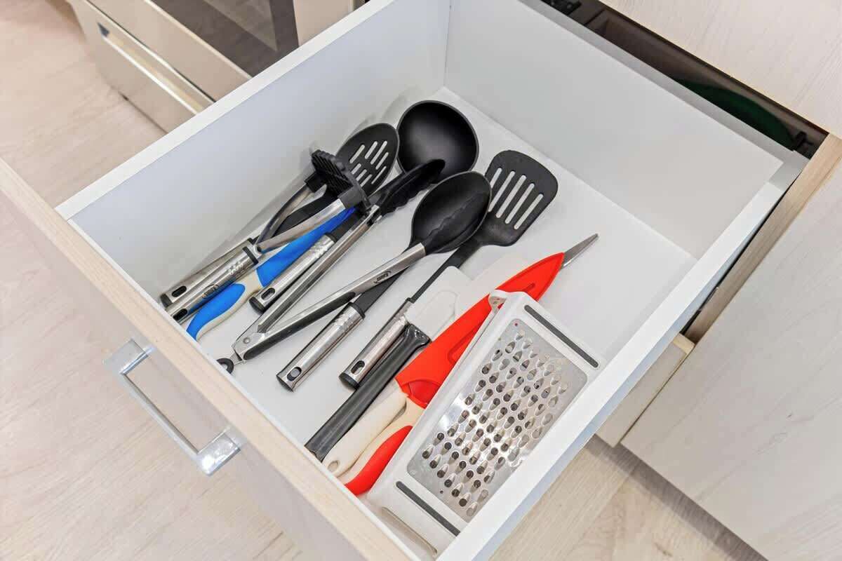 A drawer with kitchen utensils including spatulas, a grater, and a pair of scissors.