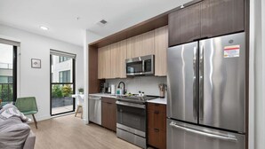 A modern kitchen with stainless steel appliances, wooden cabinets, and a sliding glass door leading to a balcony. - Studio to Downtown w Rooftop (Cincinnati)