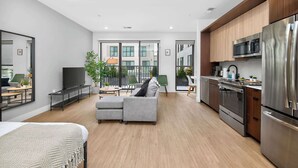 A modern kitchen with stainless steel appliances, a grey sofa, and a dining area with a table and chairs. - Studio to Downtown w Rooftop (Cincinnati)