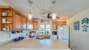Una cocina con armarios de madera, una isla central, un ventilador de techo y un refrigerador.