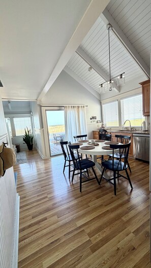 A spacious loft-style interior with a dining area, kitchen, and large windows offering views. - Bald Head Island Oceanfront Coastal Retreat with BHI club access (Bald Head Island)