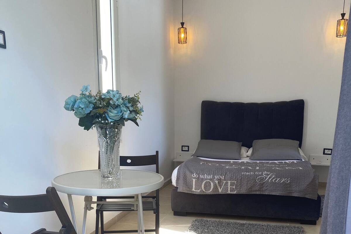 A bedroom with a bed, bedside table, and a small round table with a chair.