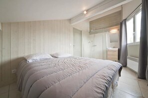 Ein Schlafzimmer mit Bett, Kleiderschrank, Spiegel und einem Badezimmer mit Dusche.