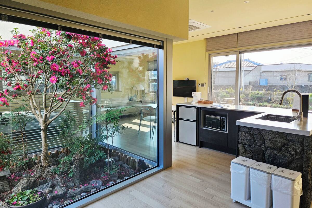 A modern kitchen with a built-in oven, a sink, and a window overlooking a garden.