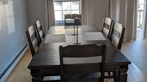 Un comedor con una mesa de madera larga, seis sillas, una lámpara de pie y un equipo de aire acondicionado.