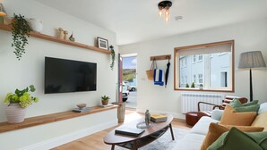Een woonkamer met een flatscreen televisie, houten planken, een bank en een raam met uitzicht.