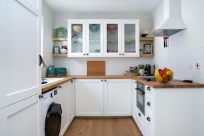 Una cocina con armarios blancos, encimera de madera, horno empotrado y lavavajillas.