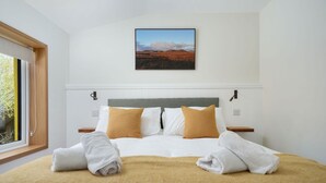 Een hotelkamer met een bed, een raam, een schilderij aan de muur en uitzicht op het omliggende landschap.