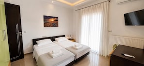 A hotel room with two beds, a TV, a desk, and a painting of a sunset. - Rhodian Villa - Three Bedroom Villa, Sleeps 6 (Kremasti)