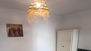 Une pièce avec un lustre, une armoire blanche, une chaise noire, une petite table avec une boîte, et un lit avec une couverture.