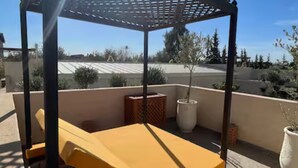 Une terrasse extérieure ensoleillée, avec une table et des chaises jaunes, entourée de plantes en pot et d’une pergola.