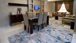 A modern living room with a dining area, a flat-screen TV, and a patterned rug. - ALSAWAH 3BR Garden Apartment - New Cairo (New Cairo)
