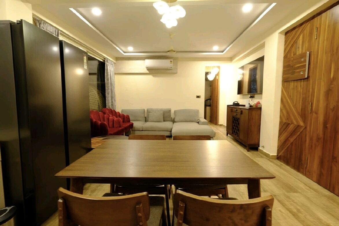 A dining area with a wooden table and chairs, a sofa, and a kitchen area with cabinets and a refrigerator.