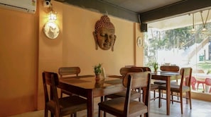 Un comedor con una escultura de cabeza de Buda, una lámpara de pared y vistas a una escalera y vegetación exterior.