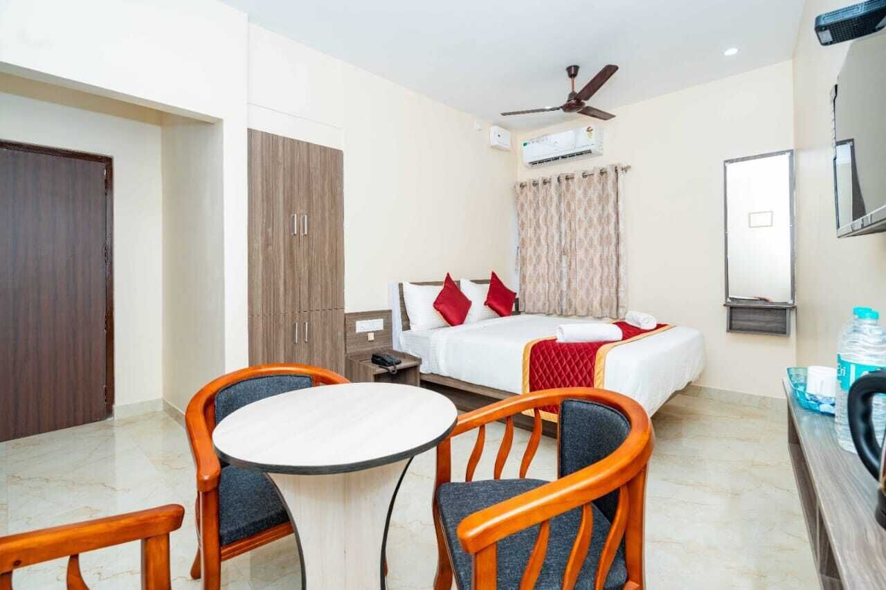 A hotel room with a bed, a table with chairs, a ceiling fan, an air conditioning unit, and a television.