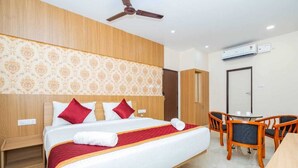 Ein Hotelzimmer mit einem Bett, einem Schreibtisch, Stühlen, einem Deckenventilator und einer Klimaanlage.