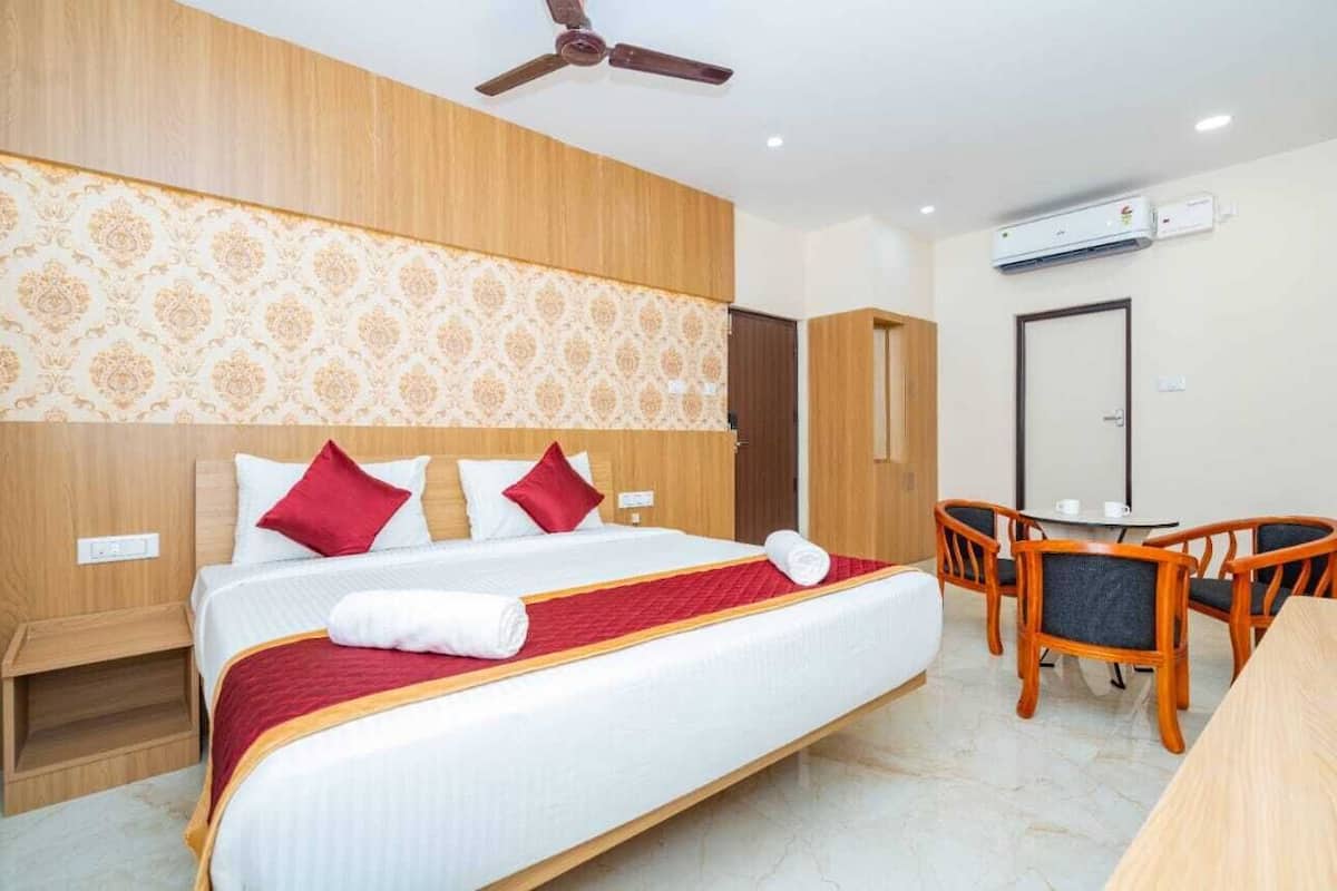 A hotel room with a bed, a desk, chairs, a ceiling fan, and an air conditioning unit.