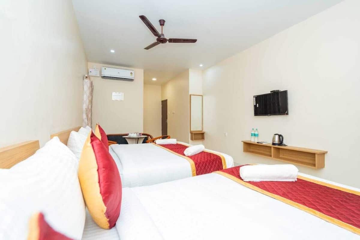 A hotel room with two beds, a ceiling fan, a TV, a small table, and a shelf with toiletries.