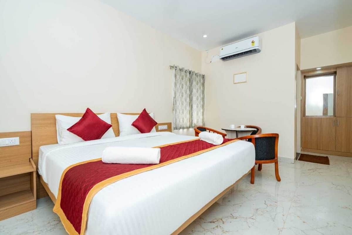 A hotel room with a bed, a desk, a chair, a wardrobe, and an air conditioning unit.