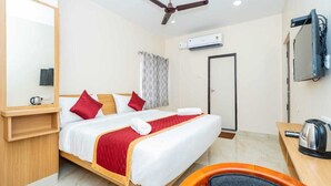 Ein Hotelzimmer mit Bett, Schreibtisch, Stuhl, Deckenventilator, Klimaanlage und Fernseher.