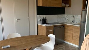 Uma cozinha compacta com uma mesa de madeira, cadeiras brancas e uma geladeira.
