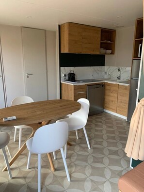 A compact kitchen with a wooden table, white chairs, and a refrigerator. - Camping 4 étoiles - Parc aquatique - eeidec (Valras-Plage)