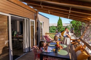 Een terras buiten met een tafel gedekt voor ontbijt, een houten pergola en een schuifdeur naar een kamer.